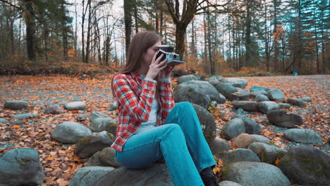 Photographer-woman-takes-Polaroid-photo-along-riverside-among-fall-colors