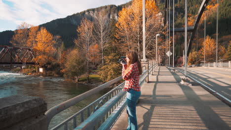 Eine-Fotografin-Macht-Ein-Polaroidfoto-Des-Tals-Von-Der-Brücke-Inmitten-Der-Herbstfarben