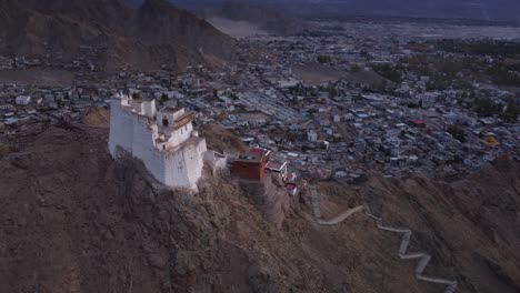 Filmische-Drohnenaufnahme-Des-Sankar-Klosters-Und-Tempels-Mit-Blick-Auf-Die-Stadt-Leh-Im-Hintergrund-Bei-Sonnenuntergang,-Ladakh,-Indien