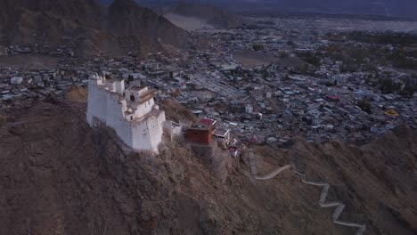 Toma-Cinematográfica-De-Un-Dron-Del-Monasterio-Y-Templo-De-Sankar-Y-La-Ciudad-De-Leh-Al-Fondo-Durante-La-Puesta-De-Sol,-Ladakh,-India