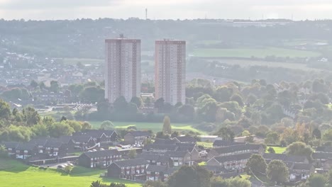 Ascending-drone-shot-showing-two-apartment-block-tower-surrounded-by-park-and-neighborhood-in-Leeds-during-cloudy-day