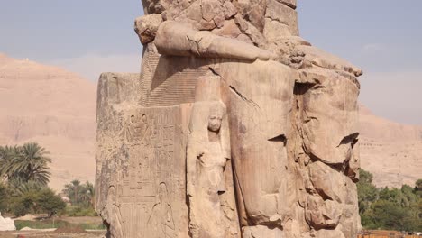 Ruinas-De-La-Estatua-Gigante-Del-Faraón-Con-Montañas-Al-Fondo-En-Los-Colosos-De-Memnon-En-Luxor,-Egipto-Con-Palmera