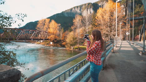 Photographer-woman-takes-Polaroid-photo-of-valley-from-bridge-among-fall-colors