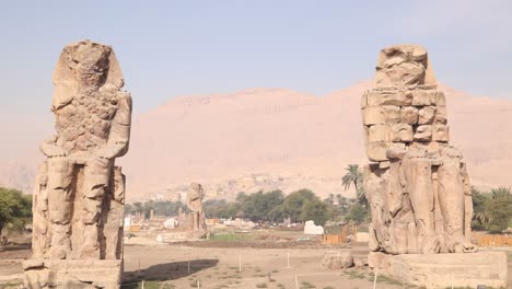 ruins-of-the-two-giant-statues-of-pharoah-with-mountains-in-the-background-at-the-Colossi-of-Memnon-in-Luxor-Egypt