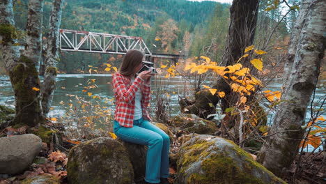 Eine-Fotografin-Macht-Ein-Polaroidfoto-Am-Flussufer-Inmitten-Der-Herbstfarben
