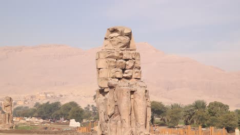 Ruinas-De-La-Estatua-Gigante-Del-Faraón-Con-Montañas-Al-Fondo-En-Los-Colosos-De-Memnon-En-Luxor,-Egipto.