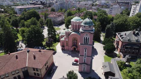 Aerial:-the-Holy-Trinity-Church-in-Banja-Luka-surrounded-by-lush-trees,-Bosnia
