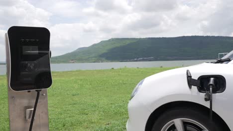 Progressive-concept-of-EV-car-with-green-field,-hill-and-lake-as-background.