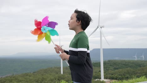 Progressive-young-asian-boy-playing-with-wind-turbine-toy-at-wind-turbine-farm.