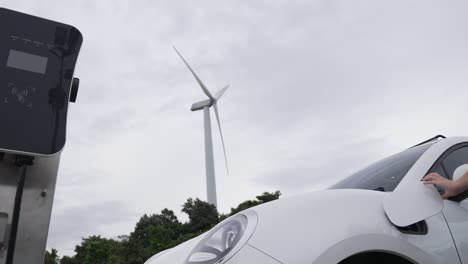 Progressive-woman-recharge-EV-from-charging-station-generated-by-wind-turbine.