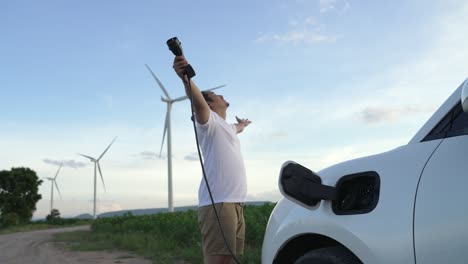 Progressive-man-with-his-EV-car-and-wind-turbine-as-concept-of-renewable-energy.