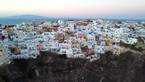 Luftaufnahmen-Von-Oia,-Santorini,-Den-Berühmten-Weißen-Häusern-Und-Blauen-Kuppeln-Am-Rande-Der-Klippe-Und-Der-Blauen-Lagune