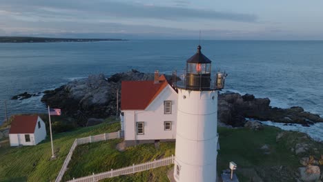 Luftdrohnenaufnahme-Von-York-Beach-Maine,-Der-Bei-Sonnenuntergang-Um-Den-Cape-Neddick-Nubble-Lighthouse-Fliegt