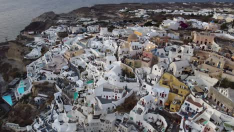 Luftaufnahmen-Von-Oia,-Santorini,-Den-Berühmten-Weißen-Häusern-Und-Blauen-Kuppeln-Am-Rande-Der-Klippe-Und-Der-Blauen-Lagune