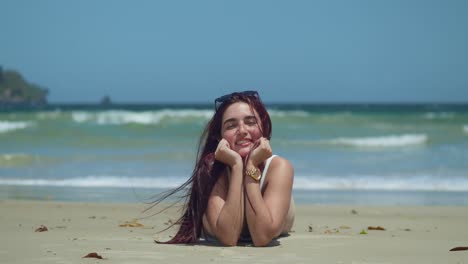 Hispanic-red-hair-girl-laying-in-a-white-sand-beach-with-ocean-waves-in-the-background
