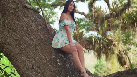 Young-girl-sits-on-a-large-tree-trunk-in-a-short-dress-in-a-park-on-a-sunny-day