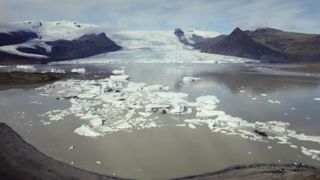 Aerial-fly-over-dramatic-icebergs-floating-in-water,-Jokulsarlon-lake,-natural-climate-snow-landscape-view,-Iceland