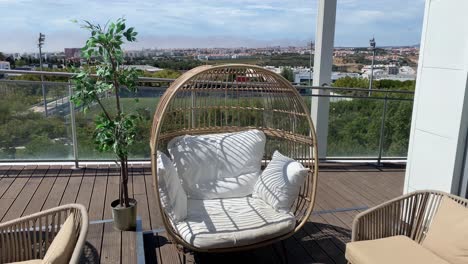 Rattan-egg-chair-with-white-cushions-and-pillows-on-the-terrace-overlooking-the-city