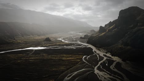 Dramatic-aerial-thor-valley,-glacial-river-flowing-through-black-volcanic-mountain,-thorsmörk-cinematic-moody-Iceland