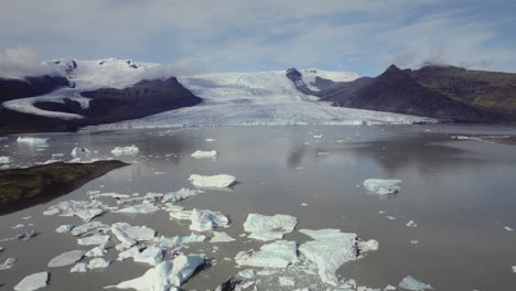 Aerial-flying-over-dramatic-icebergs-floating-in-water,-Jokulsarlon-lake,-natural-climate-snow-landscape,-Iceland