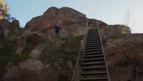 Eine-Panoramaaufnahme-Zeigt-Eine-Treppe-Entlang-Eines-Berghangs,-Einen-Mann,-Der-An-Einem-Aussichtspunkt-Steht,-Blauen-Himmel-Und-Moos,-Das-Auf-Der-Sandsteinfelsenformation-Wächst