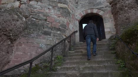 A-man-walking-up-stone-steps-to-an-archway-in-an-ancient-brick-building,-castle-or-fortress