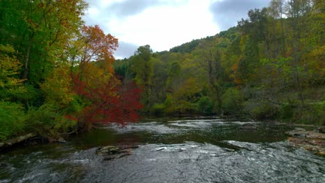 Drone-glides-over-a-running-river-in-the-mountains-of-North-Caroline-in-the-fall-with-colorful-leaves-painted-in-the-background