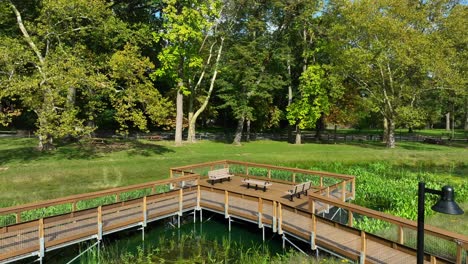 Wooden-boardwalk-with-benches-over-lush-green-wetland-in-a-serene-park-setting