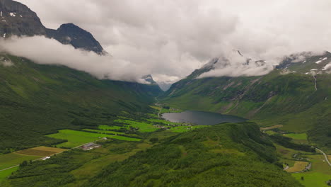 Stunning-nordic-valley-with-low-hanging-clouds-and-alpine-lake-by-farm-plots
