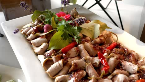 Platter-with-deli-meat-in-sauce,-accompanied-by-chili-peppers,-grapes,-and-herbs