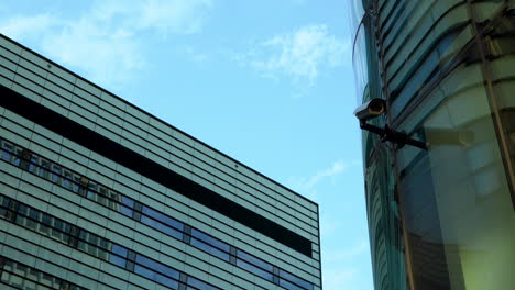 Moderne-Gebäude,-Die-Sich-Schräg-überschneiden,-Mit-Einer-Überwachungskamera-Im-Vordergrund-Vor-Blauem-Himmel