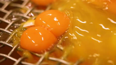 Close-up-of-many-egg-yolks-falling-through-a-small-mesh-or-hole-in-a-factory