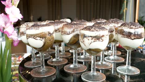 Elegante-Gläser-Mit-Einem-Bunten-Tiramisu-Dessert-Auf-Einem-Tisch-Angeordnet
