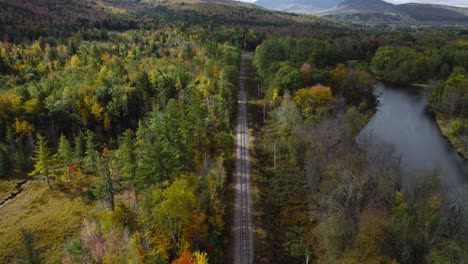Flying-over-railroad-track-near-river-during-colorful-autumn-forest