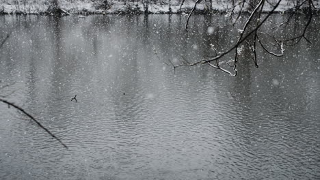 View-from-riverbank-of-snow-falling-into-river-in-slow-motion