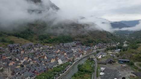 The-drone-initiates-with-a-view-of-the-quaint-Spanish-town-in-the-Pyrenees-mountains-and-then-smoothly-pans-to-unveil-the-cloudy,-majestic-mountain-landscape-of-the-Pyrenees