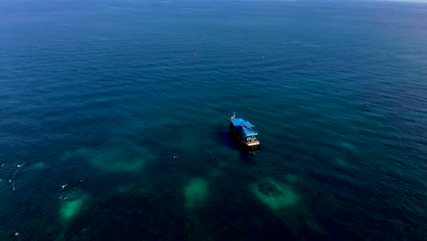 A-partial-orbit-aerial-drone-shot-panning-from-left-to-right-of-some-tourists-snorkeling-in-the-deep-blue-waters-of-the-Andaman-Sea-near-Koh-Tao-in-Surat-Thani-province-in-Thailand