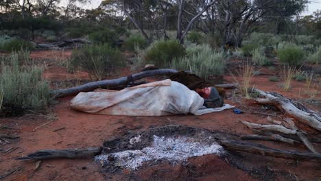 A-bushman-sleeping-in-his-historical-oil-skin-swag-in-the-Australian-outback-next-to-a-fire-place