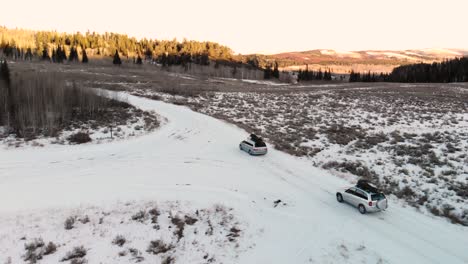Aerial-decent-of-cars-driving-in-snow-with-Christmas-trees-in-Idaho-National-Forest-during-a-winter-sunset