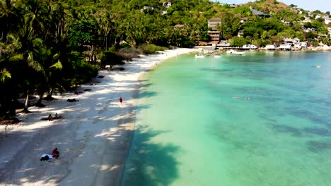 A-slow-aerial-drone-shot-approach-of-Shark-Bay,-showing-its-white-sandy-beach,-crystal-blue-waters,-and-with-tourists-relaxing-at-the-beachfront-in-the-island-of-Koh-Tao,-Surat-Thani,-Thailand