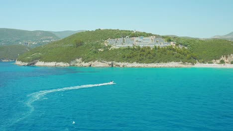 Luftaufnahme-Des-Türkisfarbenen-Karavostasi-Strandwassers-Mit-Einem-Schnellboot,-Das-Touristen-In-Einem-Schlauchboot-Schleppt,-Griechenland