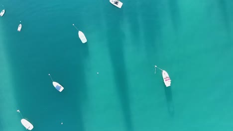 Birds-Eye-Aerial-Shot-of-Small-Boats-Anchored-and-Driving-in-Light-Blue-Turquoise-Tropical-Water-near-Beach-with-Lido-and-Swimmers