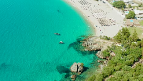 Topdown-view-of-Karavostasi-Beach-scenic-water,-pullback-tilt-up-revealing-Exclusive-Hotel-Elix-Mar-Bella,-Greece