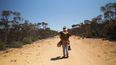 A-historical-looking-swagman-stand-on-a-remote-outback-road-in-Australia