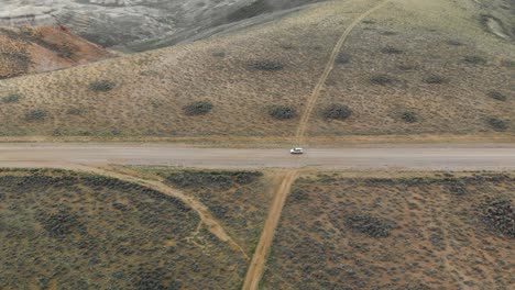 Luftverfolgung-Des-Autos-Mit-Schwenk-Enthüllung-Auf-Unbefestigter-Straße-Am-Pilot-Butte-Wild-Horse-Scenic-Loop,-Wyoming,-USA,-Mit-Weitem-Blick-Auf-Die-Schlucht