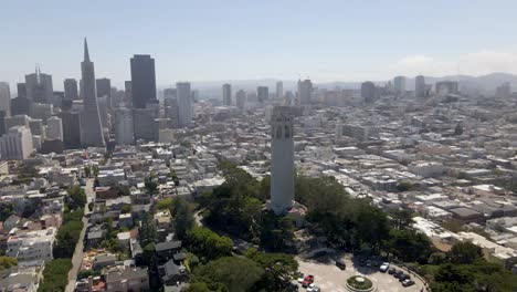 Eine-Faszinierende-Drohne-Aus-Der-Ferne-Fängt-Einen-Gemächlichen-Kreis-Um-Den-Coit-Tower-In-San-Francisco-Ein,-Wobei-Sich-Der-Hintergrund-Von-Den-Wolkenkratzern-In-Der-Innenstadt-In-Den-Malerischen-Nördlichen-Teil-Der-Stadt-Verschiebt