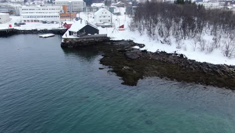 Drone-still-view-in-Tromso-area-flying-over-sea-in-winter-looking-at-Finnsnes-small-town-with-a-hotel-on-the-shore-in-Norway