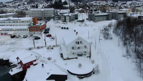 Drone-view-in-Tromso-area-flying-over-Finnsnes-in-winter-and-showing-the-sea-next-to-the-snowy-town-with-a-hotel-in-Norway