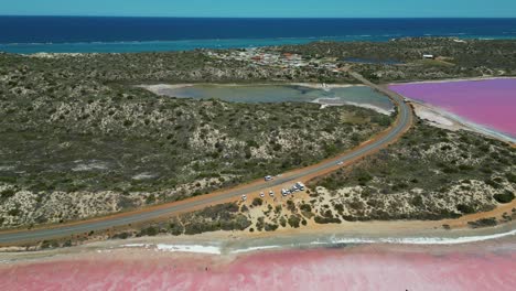 Aerial-view-looking-over-the-road-and-shoreline-of-Pink-Lake,-Hutt-Lagoon,-Western-Australia
