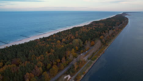 Aerial-view-of-a-narrow-strip-of-land-with-road,-forest,-and-sea-on-both-sides-at-dusk